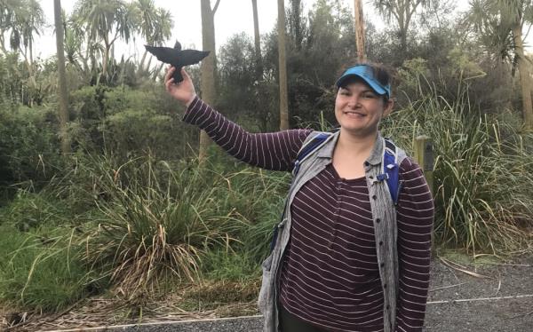 A woman stands in front of native vegetation holding up a 3D-printed swallow outline.